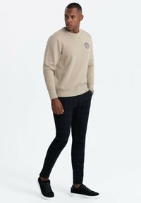 Sudadera beige con cuello redondo y puños acanalados, combinada con pantalones de cuadros en azul marino y zapatillas negras.