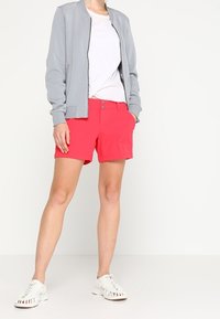 Světlounce šedá bomber bunda, bílé tričko a jasně růžové šortky. Bílé casual boty. Hladká tkanina, volný střih a minimalistický design.