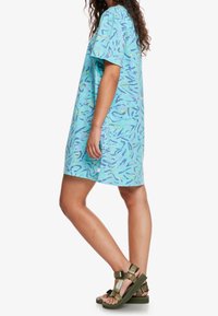 Robe bleu clair à manches courtes avec un motif abstrait coloré, longueur genou, en matériau doux. Associée à des sandales épaisses vert olive.