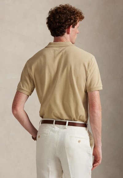 Κοντομάνικο πόλο με κλασικό γιακά και υφή, φορεμένο με παντελόνι κρεμ και καφέ δερμάτινη ζώνη.