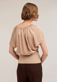 Top corto in satin beige chiaro con vestibilità rilassata, collo arricciato e vita elasticizzata, abbinato a pantaloni marrone scuro.