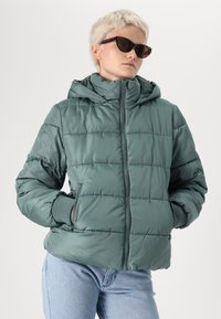 Naduvena tirkizna jakna s kapuljačom, s prednjim zatvaračem, bočnim džepovima i rebrastim manžetama. Glatka tekstura s horizontalnim quilted uzorkom.