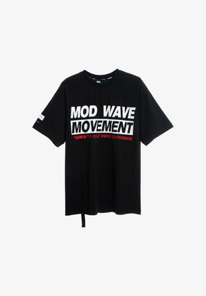 Joven con camiseta negra "Mod Wave Movement", shorts vaqueros con parche de oso, calcetines blancos con estampado y deportivas negras texturizadas, de pie sobre fondo blanco.