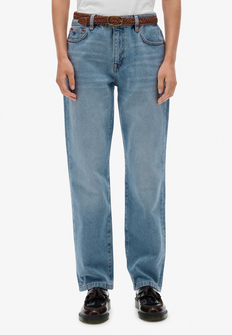 Jeans de algodón de mezclilla azul claro con corte relajado, forma recta, cinco bolsillos y un cinturón de piel trenzada marrón. También incluye unos zapatos marrones.