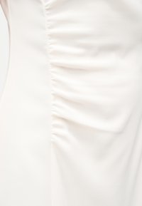 Λευκό ύφασμα με κάθετη λωρίδωση που δημιουργεί ρυτιδωτή υφή κατά μήκος της κεντρικής ραφής.