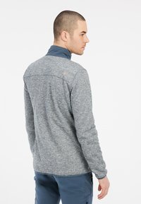 Grijze textuur fleecejack met een staande kraag, voorzien van een contrasterende blauwe binnenkraag en subtiele branding op de achterkant.