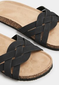 Sandali neri in ecopelle con design a strappo intrecciato, dotati di una soletta imbottita color tan e una suola in sughero testurizzato.