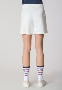 Shorts bianchi, a metà coscia, con vita elasticizzata, abbinati a calzini bianchi con righe rosse e blu navy e dettagli con logo.