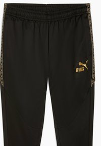 Svarta sportbyxor i slät tyg, med en gul logotyp och mönstrade sidodetaljer, samt resårmidja och avsmalnande ben.