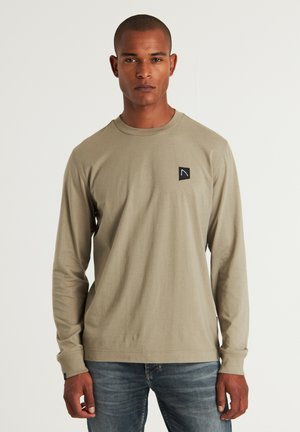 Langarmshirt in hellem Olivgrün, aus weichem Material, mit einem kleinen schwarzen Logo-Patch auf der linken Brust. Schlichtes Design, runder Ausschnitt.