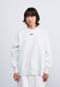 Sweatshirt gris clair en tissu doux, avec un col rond et des poignets côtelés, arborant un petit logo Nike noir sur la poitrine.