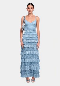 Vestito a balze azzurro chiaro con corpetto aderente e strati arricciati, realizzato in tessuto strutturato con un motivo sottile. Accessori argento completano il look.