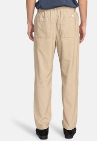 Beige, relaxed-fit pants with an elastic waistband and two back pockets. Material appears textured and lightweight, suitable for casual wear.