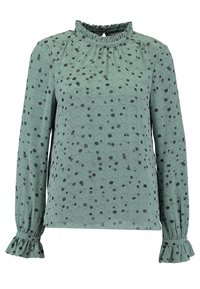 Blouse verte à manches longues avec pois noirs, col à volants et poignets évasés en tissu léger. Présente des épaules légèrement froncées.