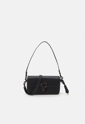 Schwarze Lederschultertasche mit Klappverschluss, Metallverschluss und verstellbarem Riemen vor einfachem hellem Hintergrund.