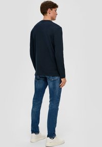 Granatowa koszula z długim rękawem okrągłym dekoltem, zestawiona z dopasowanymi niebieskimi dżinsami i białymi sneakersami. Prosty design bez widocznych wzorów.