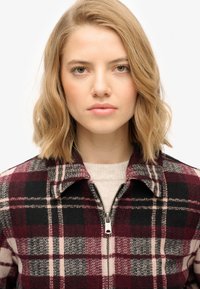 Kurtka w kratę w odcieniach burgundu, czerni i szarości. Posiada zamek błyskawiczny i kołnierz, wykonana z miękkiego, teksturowanego materiału.