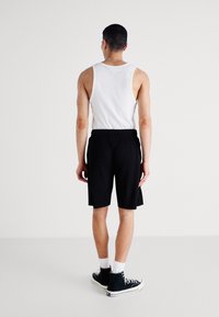 Pantalones cortos negros a rayas con cintura elástica y bolsillos laterales, combinados con una camiseta sin mangas blanca y zapatillas altas negras.