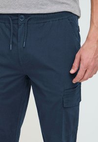 Navyblauwe cargobroek van lichtgewicht stof, met een elastische tailleband en trekkoord, en een zijzak met klep.