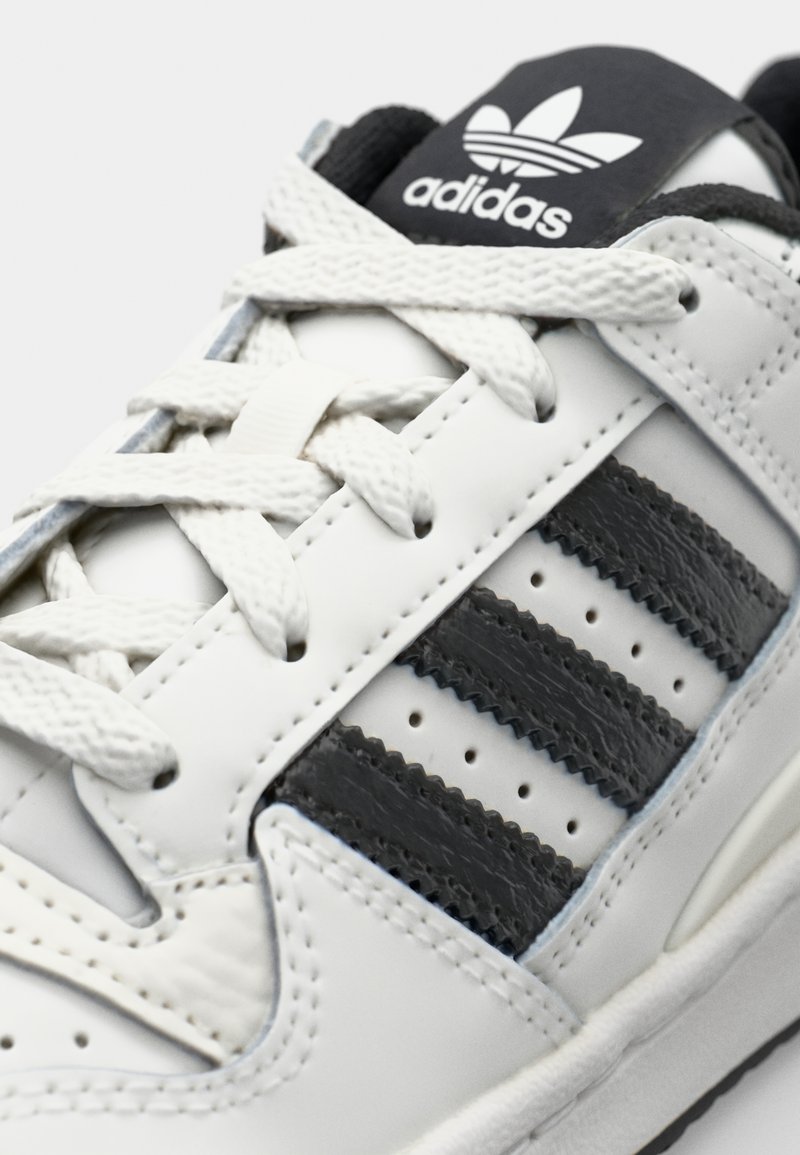 Witte sneaker met zwarte accenten, voorzien van drie horizontale stripes, textuurleer, vetersluiting en een zwarte gemerkte tong.