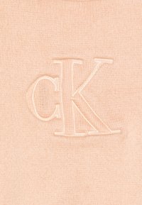 Knit fabric w kolorze brzoskwiniowym ma wytłoczone logo "CK" w jaśniejszym odcieniu. Tekstura jest gładka z delikatnym prążkowanym wzorem.