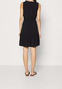 Svart ärmlös klänning med en samlad midja, lager på lager fåll och subtila volangdetaljer vid halslinningen, tillverkad av lättviktsmaterial.