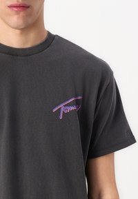 Grå bomullströja med rund halsringning, korta ärmar och en rosa och lila grafisk design på vänster bröstområde.