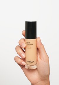 Fond de teint Insta Moisture de KIKO Milano dans un flacon en verre transparent avec un bouchon noir, présente une couleur beige clair et une étiquette SPF 25.