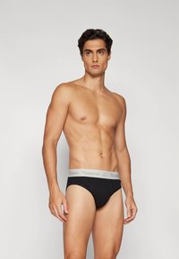 Fekete pamut férfi alsónadrág szürke, márkás derékpánttal. Klasszikus szabással és sima textúrával rendelkezik. A modell semleges pózban áll.