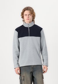 Pullover in pile grigio con colletto e pannelli superiori blu navy. Presenta una zip a quarto, una texture morbida, maniche lunghe e una vestibilità rilassata.