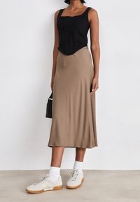 Czarny dopasowany top z teksturowanej tkaniny, zestawiony z luźną beżową spódnicą midi. Modelka ma na sobie beżowe sneakersy i białe skarpetki sięgające do kostek.
