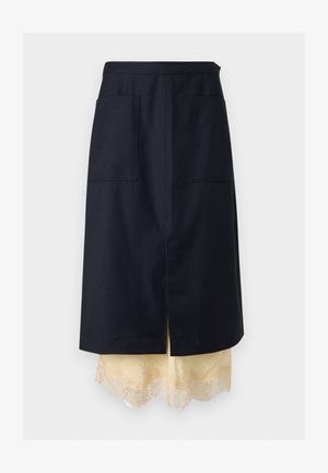 Laivastonsininen A-linjainen hame etutaskuilla, kerroksittain kermanvärisen pitsireunaisen alusmekon päällä, keskellä halkio, esitetty yksivärisellä taustalla.