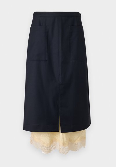 Σκούρα μπλε φούστα σε γραμμή Α με μπροστινές τσέπες, στρωμένη πάνω από κρεμ underskirt με δαντέλα, κεντρικό σκίσιμο, παρουσιασμένη σε μονόχρωμο φόντο.