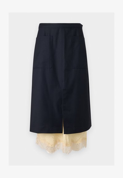 Σκούρα μπλε φούστα σε γραμμή Α με μπροστινές τσέπες, στρωμένη πάνω από κρεμ underskirt με δαντέλα, κεντρικό σκίσιμο, παρουσιασμένη σε μονόχρωμο φόντο.