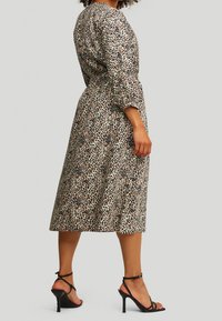 Robe midi à imprimé léopard avec manches trois-quarts et taille cintrée, confectionnée dans un tissu léger. Associée à des sandales à talons noires.