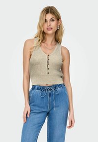 Beige geribbelde gebreide mouwloze top met een V-hals en vijf bruine knoopsluitingen, gecombineerd met lichtblauwe denim broek met trekkoord.