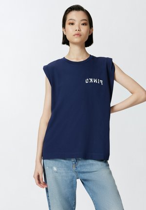 Camiseta sin mangas de color marino hecha de algodón, con cuello redondo y estampado del logo. Combinada con jeans desgastados de color azul claro.