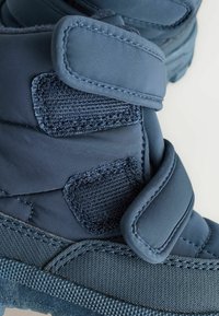 Blaue Stoffstiefel mit zwei Klettverschlüssen, gepolsterten Flächen und strukturierten Akzenten, die ein robustes, leichtes Design betonen.