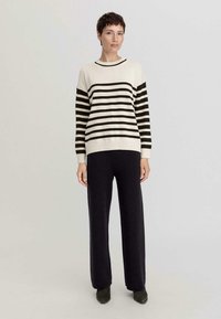 Gestreifter Pullover in Creme und Dunkelbraun, gestrickte Textur, runder Ausschnitt, kombiniert mit dunklen Hosen. Der Pullover hat lange Ärmel und einen gerippten Saum.