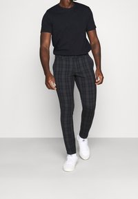 Svart t-shirt tillsammans med figurnära mörka skotska byxor med en rutigt mönster i marinblått och brunt, kompletterat med vita sneakers.