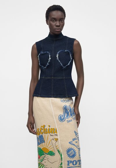 Γυναίκα που φοράει ένα σκουρόχρωμο denim τοπ χωρίς μανίκια με φθαρμένες καρδιές και μια μπεζ φούστα με πολύχρωμα γραφικά σχέδια.