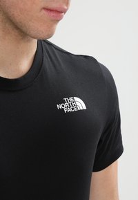 Černé tričko s krátkým rukávem vyrobené z měkké látky, s bílým logem "The North Face" na levé straně hrudi.
