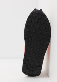 Svart gummisula med upphöjda fyrkantiga punkter för grepp, utrustad med en texturerad yta och patentmarkeringar. Accenterad med en röd kant.