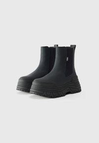 Botines Chelsea negros hasta el tobillo, hechos de material texturizado, con paneles laterales elásticos, suelas de plataforma gruesa y un diseño de punta redondeada.