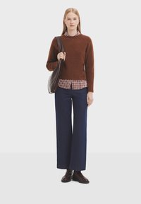 Brauner Strickpullover mit Rippstruktur, über einem rot-weiß gestreiften Shirt getragen. Kombiniert mit dunkelblauen weit geschnittenen Hosen und braunen Stiefeln.