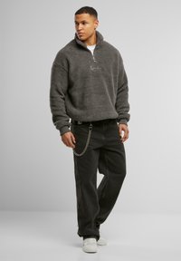Grå, fluffy fleece-genser med halv-glidelås og broderte detaljer. Kombinert med svarte jeans og et sølvkjede. Hvite sneakers.