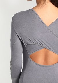 Szary top z długim rękawem, o fasonie kopertowym z detalem odkrytych pleców, wykonany z gładkiej, elastycznej tkaniny o subtelnym połysku.