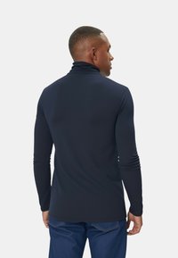 Dolcevita a maniche lunghe blu navy realizzato in materiale liscio ed elastico, con un design aderente e dettagli minimi sulle cuciture, abbinato a jeans di denim.