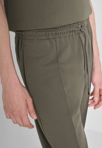 Pantalones jogger verde oliva hechos de una suave mezcla de algodón, con una cinturilla elástica con cordón y bolsillos laterales para mayor comodidad.