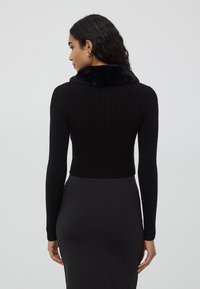 Czarny sweter prążkowany z futrzanym kołnierzem, krótki fason, długie rękawy, w połączeniu z czarną dopasowaną spódnicą. Gładka tekstura.